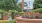a brick wall with a brick walkway and plants and a building